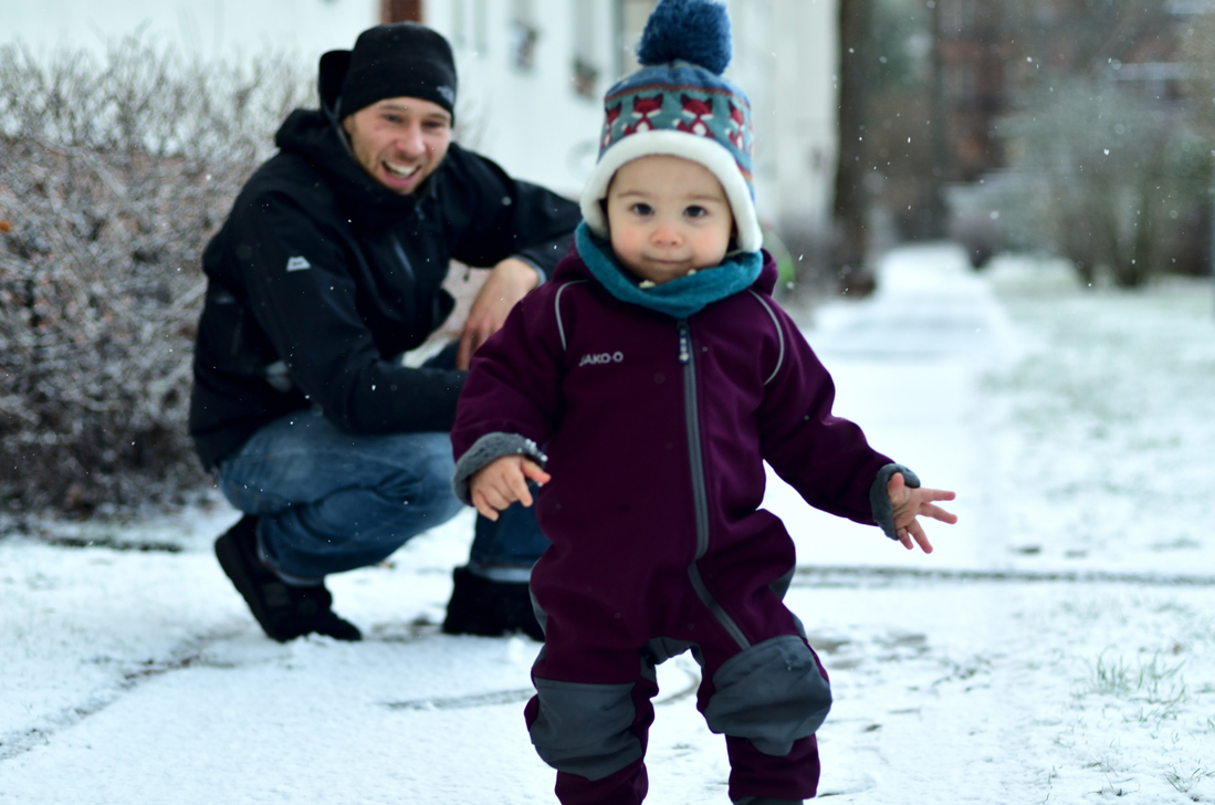 Ein kleiner erst 1 Jahr alter Junge entdeckt das alleine Laufen und den ersten Schnee seines Lebens während sein Papa im Hintergrund aufpasst und sich freut