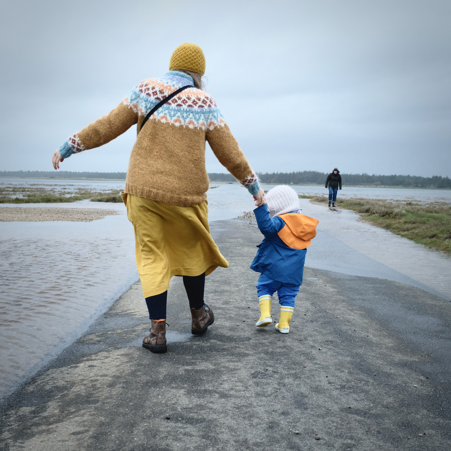 Junge Frau mit kleinem Kind in gelb und blau an einer überfluteten Straße an der Küste